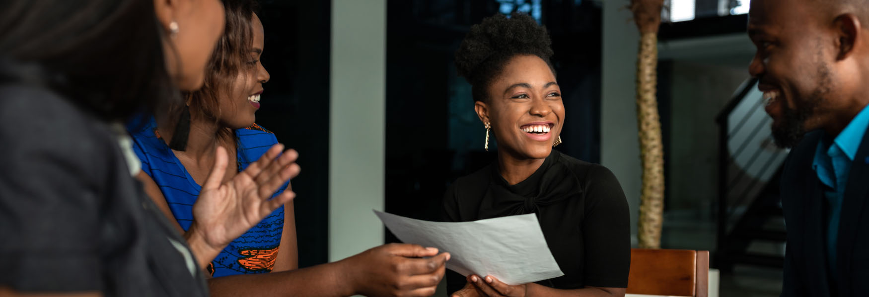 A hand reaches for violet leaves in a garden as the other hand holds a small handmade wooden basket with a rope-like handle.